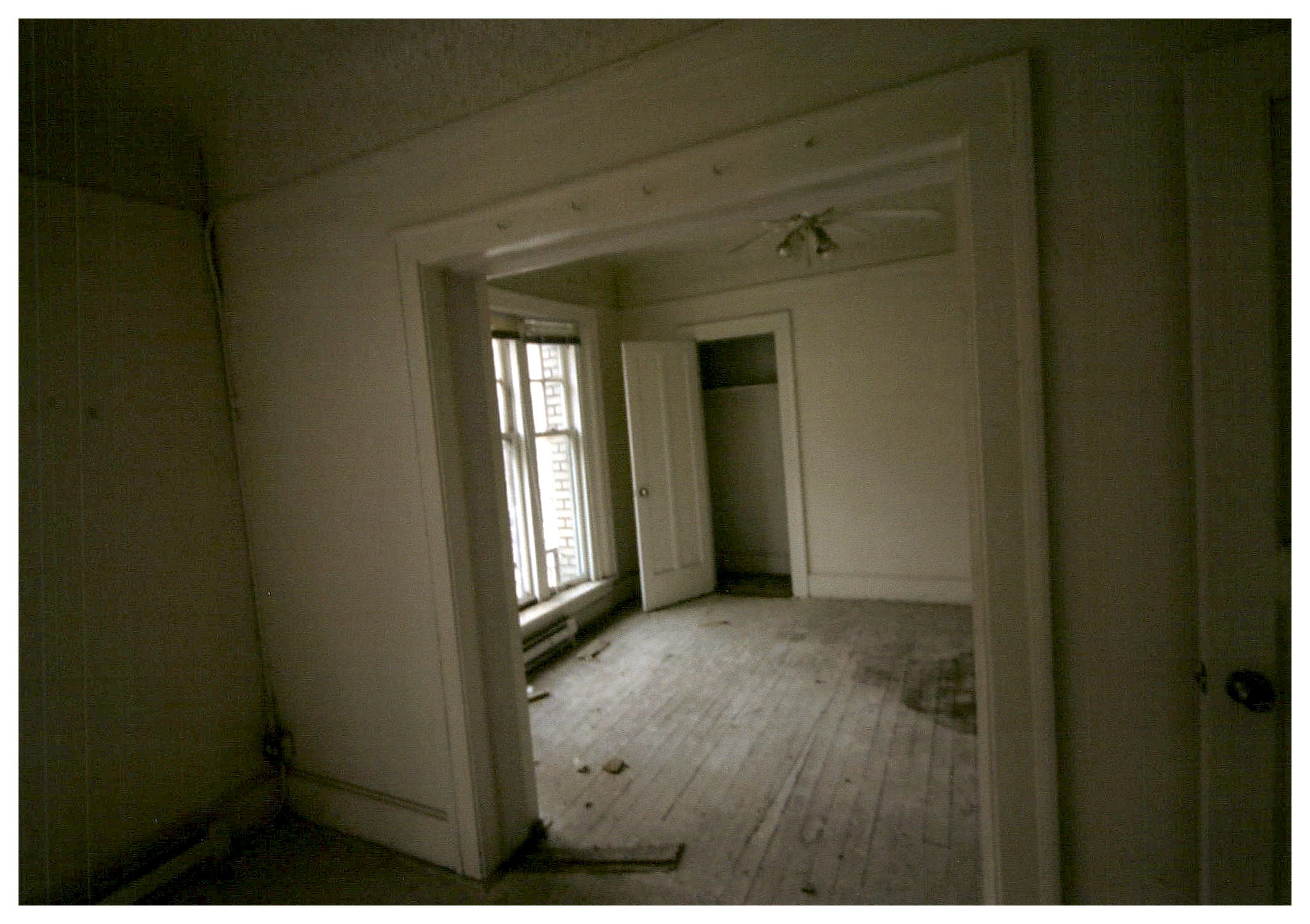 Before: view of living area from bedroom showing poor condition of wood floor.